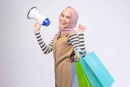 Young beautiful muslim woman in suit holding colorful shopping bags over white background studio photo
