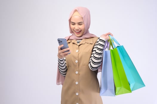 Young beautiful muslim woman in suit holding colorful shopping bags over white background studio photo