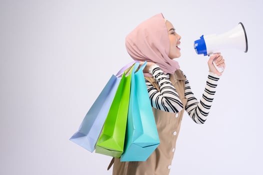 Young beautiful muslim woman in suit holding colorful shopping bags over white background studio photo