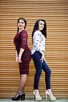 Two young teenages girl posed against orange shutter. Plump girl vs thin. photo
