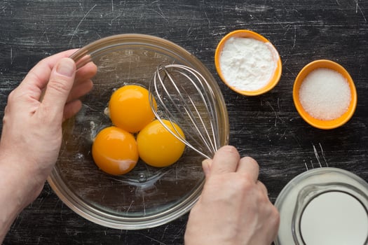 Hands holding whisk and bowl with three yolks photo