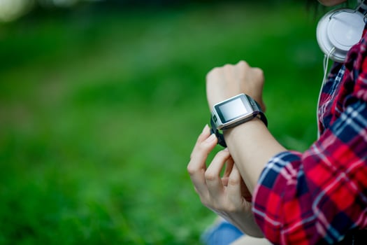 The girl watches the watch in hand, watches the time in a black watch, wears a red shirt and a green background. And there is a copy space. photo