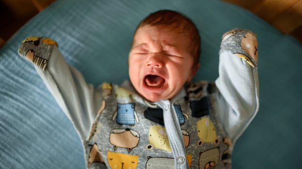 A little newborn boy is looking at the window in his crib. A boy born at 8 months of gestation. There is a knitted suit on the boy. photo