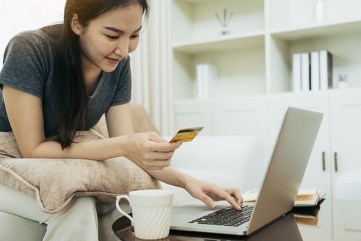 Asian woman holding a credit card for online shopping while sitting on the couch while on vacation at home. photo