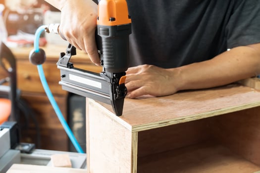 carpenter using nail gun or brad nailer tool on wood box in a workshop ,furniture restoration woodworking concept. selective focus photo