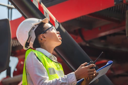 Woman Foreman in hardhat and safety vest holding holding clipboard checklist and talks on two-way radio control loading containers box from cargo photo