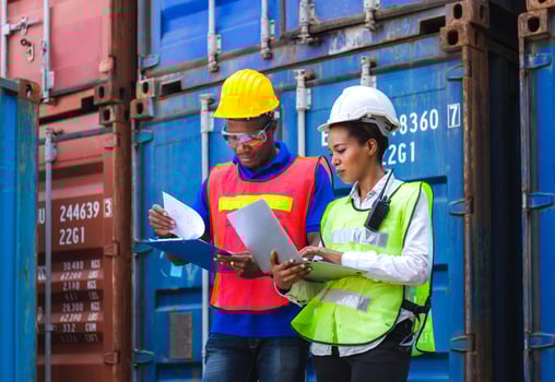 Happy worker man in hardhat and safety vest holding clipboard checklist and Female foreman using laptop control loading containers box from cargo photo