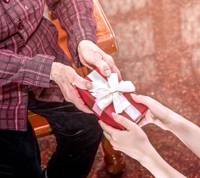 Teenage asia girl is giving grandma sitting on chair beautiful giftbox for mothers day birthday celebration idea at home with dark background, close up, copy space, cropped view photo