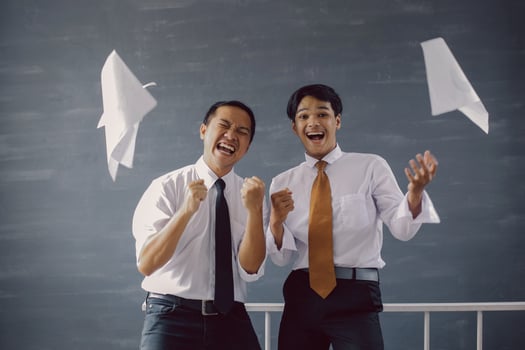 Two happy Asian businessmen celebrating their success and achievements with sheets of paper flying around them photo