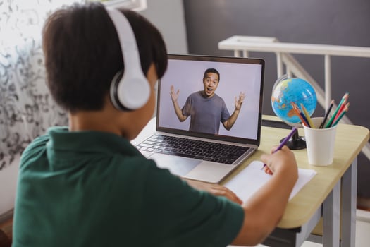 A schoolboy is writing on a paper and watching his teacher on a laptop photo
