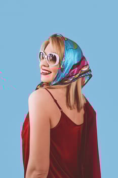 stylish smiling cheerful fancy blonde woman with make up in neckerchief and sunglasses on blue background photo