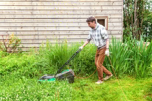 Man cutting green grass with lawn mower in backyard. Gardening country lifestyle background. Beautiful view on fresh green grass lawn in sunlight, garden landscape in spring or summer season. photo