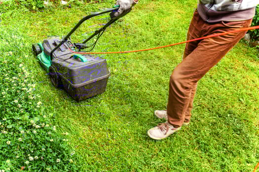 Man cutting green grass with lawn mower in backyard. Gardening country lifestyle background. Beautiful view on fresh green grass lawn in sunlight, garden landscape in spring or summer season. photo