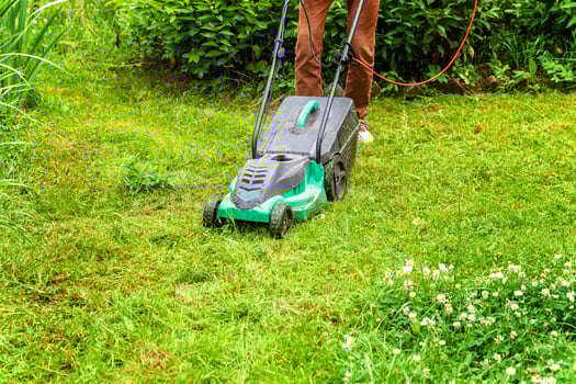 Man cutting green grass with lawn mower in backyard. Gardening country lifestyle background. Beautiful view on fresh green grass lawn in sunlight, garden landscape in spring or summer season. photo