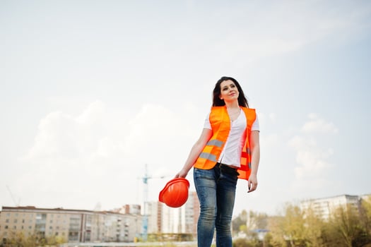 Engineer builder woman in uniform waistcoat and orange protective helmet against new buildings. photo