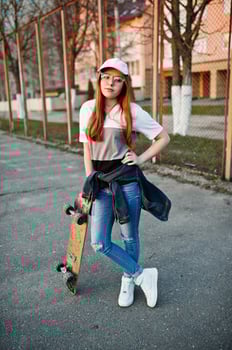 Young teenage urban girl with skateboard, wear on glasses, cap and ripped jeans at the yard sports ground. photo