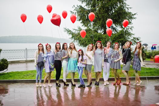 Eleven amazingly-looking braidsmaids with stunning bride posing with red heart-shaped balloons on the pavement against the lake in the background. photo