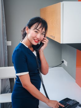 Asian woman chambermaid in uniform speaking on room telephone during work. She smiles and looking at the camera takes orders from the hotel administrator. photo