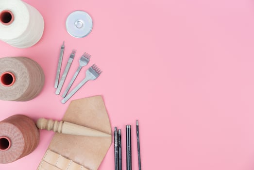 Top view with copy space of leather craft tools group, waxed rope, diamond hole punch and shape punch overhead on pink pastel background, Leather craft or leather working flat lay concept photo