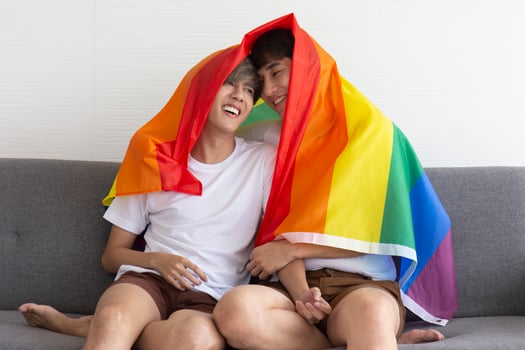 A male couple with an Asian man sitting on a sofa, holding a multicolored flag with signs of LGBT on their heads, expressing openly gay men accepting LGBT ideas. photo