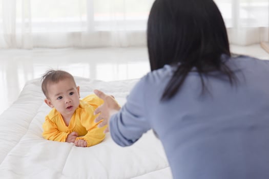 An Asian infant who is practicing crawling With her mother sitting on the other side of her soft white cloth in the bedroom photo