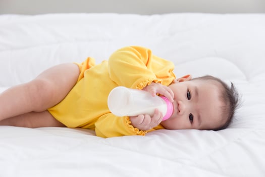 An Asian baby is sleeping on the bed and sucking the bottled milk. photo