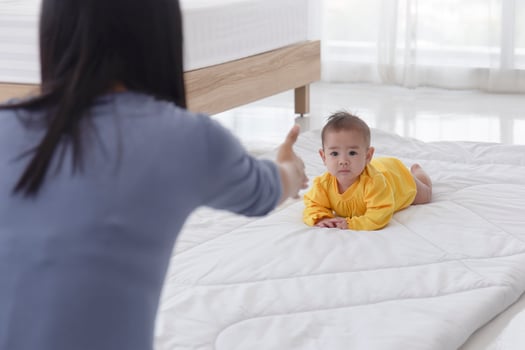 An Asian infant who is practicing crawling With her mother sitting on the other side of her soft white cloth in the bedroom photo