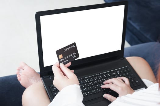 A woman holding a credit card, which is paying online, on a laptop, sitting on the sofa in the living room, at home with clipping path. The concept of online shopping.white screen notebook for mockup photo