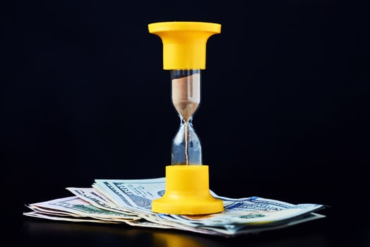Time is money or time investment and retirement saving concept. Yellow hourglass on pile of dollar bills on a dark background photo