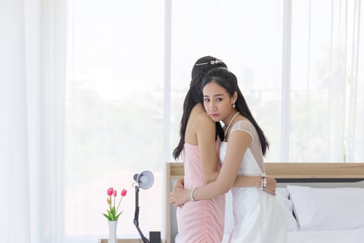 An Asian bride in a white wedding dress embraces her friend in a pink dress on her wedding day with a feeling of gratitude. photo