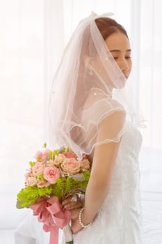 An Asian bride wore a white wedding dress, standing, holding a bouquet of beautiful flowers behind her. photo