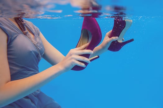 Young slim woman in gray dress holding Violet velvet shoes underwater in the swimming pool on blue background photo