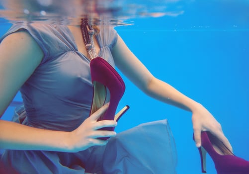 Young slim woman in gray dress holding Violet velvet shoes underwater in the swimming pool on blue background photo