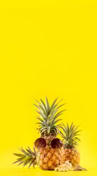 Creative pineapple looking up with sunglasses and shell isolated on yellow background, summer vacation beach idea design pattern, copy space close up photo