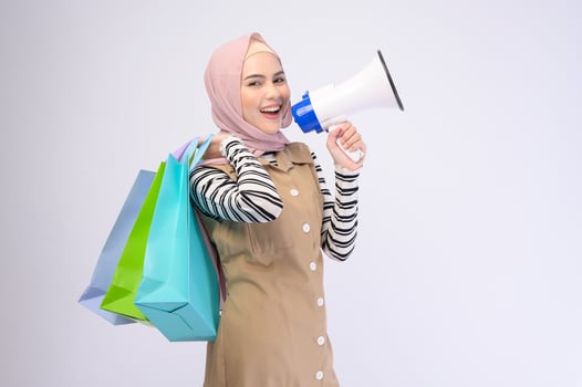 Young beautiful muslim woman in suit holding colorful shopping bags over white background studio photo