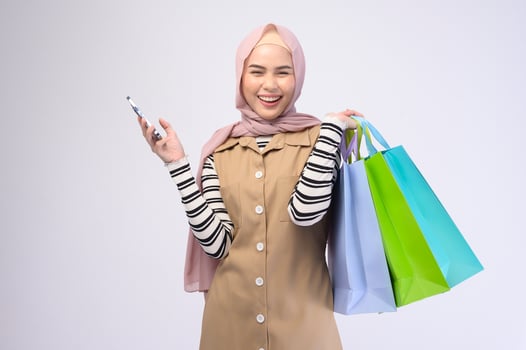 Young beautiful muslim woman in suit holding colorful shopping bags over white background studio photo