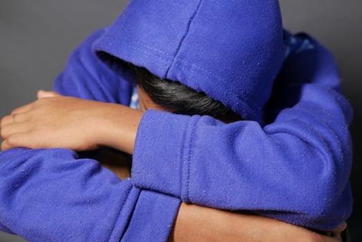 sad man in hood cover face with hands isolated in black. photo
