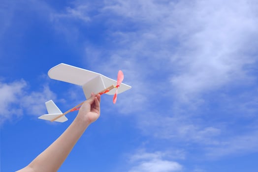 Child hand holding rubber powered aircraft up in the air against blue sky background photo