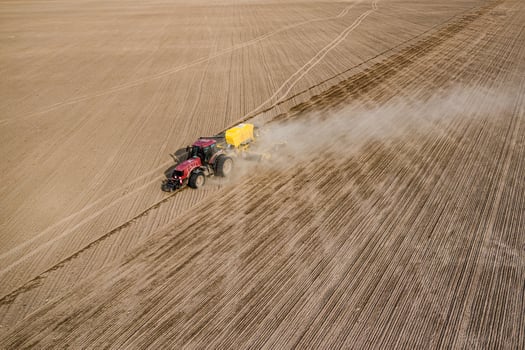 Aerial view of tractor with mounted seeder performing direct seeding of crops on plowed agricultural field. Farmer is using farming machinery for planting process, top view photo