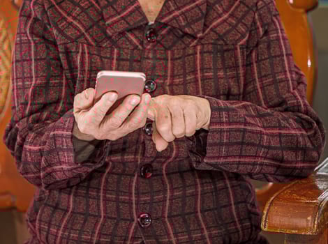 Asian elderly woman sitting and looking through something on modern smartphone, making connection with others at home, living technology, close up photo