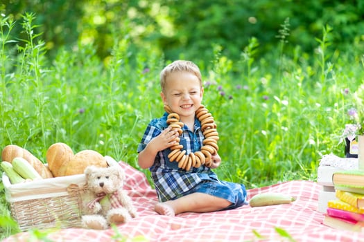 Little cute boy sits on a plaid and has fun summertime in nature. On the boys neck is a bagel necklace. photo