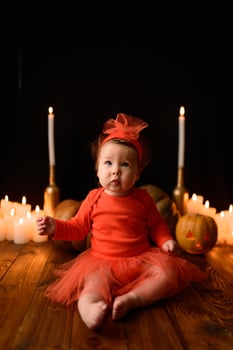 Little girl sits on a background of Jack pumpkins and candles on a black background. photo