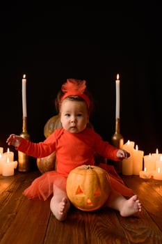 Little girl sits on a background of Jack pumpkins and candles on a black background. photo