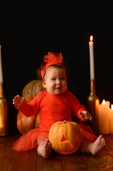 Little girl sits on a background of Jack pumpkins and candles on a black background. photo