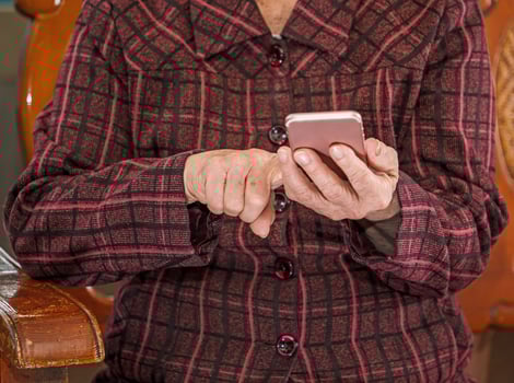Asian elderly woman sitting and looking through something on modern smartphone, making connection with others at home, living technology, close up photo