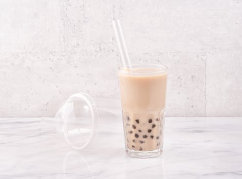 Tapioca pearl ball bubble milk tea, popular Taiwan drink, in drinking glass with straw on marble white table and wooden tray, close up, copy space. photo