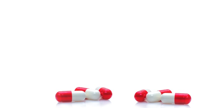 Group of red-white capsule pills on horizontal white background. Prescription drugs. Pharmacy drugstore web banner. Healthcare and medical background. Drug production. Daily dose for love booster. photo