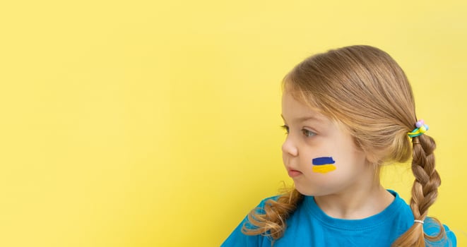 A girl with a painted Ukrainian flag of yellow and blue on her cheeks. Copy space on yellow background. photo