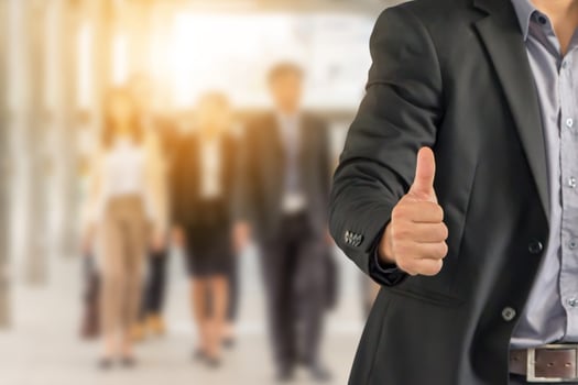 Businessman giving thumb up as sign of Success over blurred business people team background photo