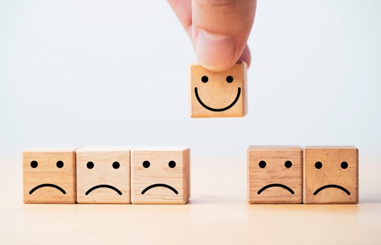 Hand holding Smile face print screen on wooden cube block among sadness face for customer service evaluation and emotion mindset concept. photo